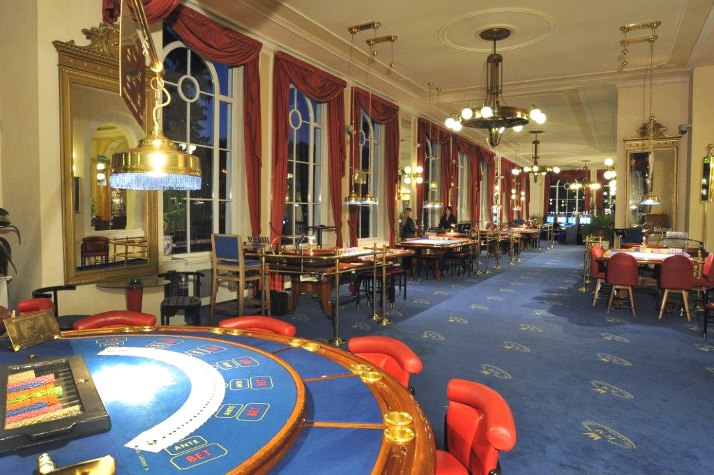 Elegante salón interior del Casino Bellevue en Marienbad, con techos altos, columnas y luz cálida de arañas de cristal